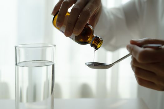 Woman hand pouring medication or cough syrup from bottle to spoon. healthcare concept