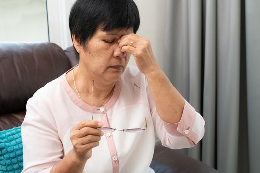 Tired old woman removing eyeglasses, massaging eyes after reading paper book. feeling discomfort because of long wearing glasses, suffering from eyes pain or headache