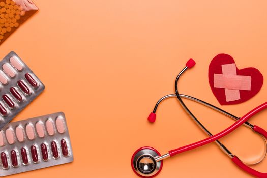 healthcare and medical concept red stethoscope and medicine on the orange background with copy space