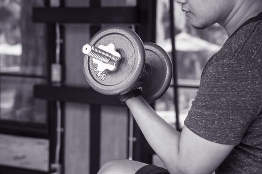 man hand lifting the steel dumbbell in a gym musclebuilding black and white image, life and fitness concept with copy space