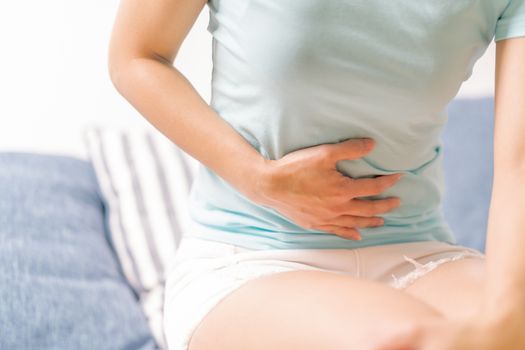 Young woman suffering from abdominal pain while sitting on the sofa and feeling stomachache, symptom of pms