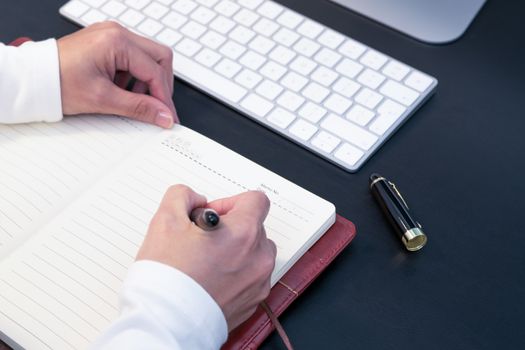 young woman writing in notebook on desktop computer and keyboard placed on working desk. Education concept