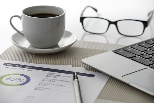 Modern workplace: a prestigious laptop, analytical prints with graphs and digital data, elegant pen, glasses and a cup of coffee