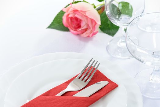 Elegant restaurant table setting for a romantic dinner with rose plates cutlery and stemware.