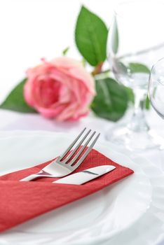 Elegant restaurant table setting for a romantic dinner with rose plates cutlery and stemware.