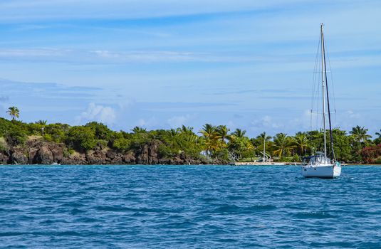 A small white sail boat anchored near the coast of a Puerto Rican island.
