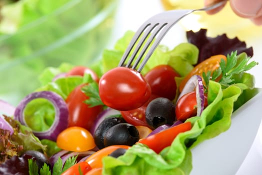 The concept of healthy nutrition - mixed vegetable salad in a bowl on the table and a hand holding a fork with tomato.