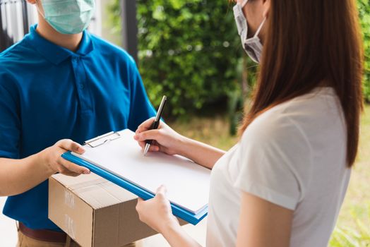 Asian young delivery man courier shopping online with package post box in uniform protective face mask coronavirus he making service woman customer using pen signature on paper book at home, COVID-19