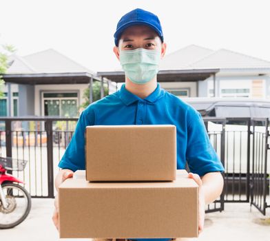 Asian delivery express courier young man use giving boxes to woman customer he wearing protective face mask at front home, under curfew quarantine pandemic coronavirus COVID-19