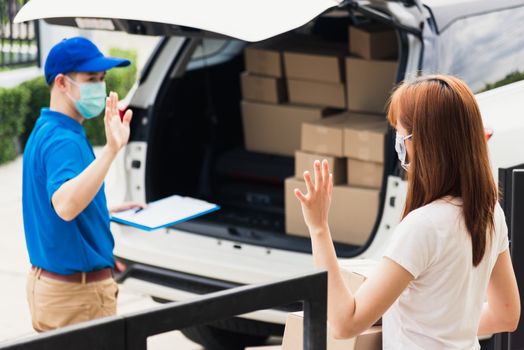 Asian young delivery man raises hand for bye after woman customer received boxes, both protective face mask under curfew quarantine pandemic coronavirus COVID-19 at front home door