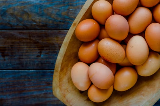 Organic eggs in a large wooden bowl on a wooden table