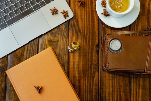 Laptop computer, tea, star anise, notebook, vintage video camera, skull rings on wooden table. Prepared to work in a warm and organized environment