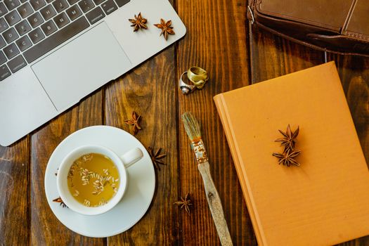 Laptop computer, tea, star anise, notebook, vintage video camera, skull rings and rusty brush on wooden table. Prepared to work in a warm and organized environment