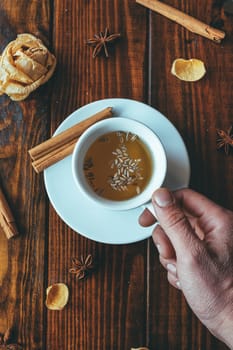 White cup of tea with one hand on a wooden table and roses around