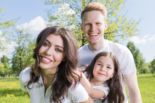 Happy family having fun outdoors in spring park against natural green meadow and trees background