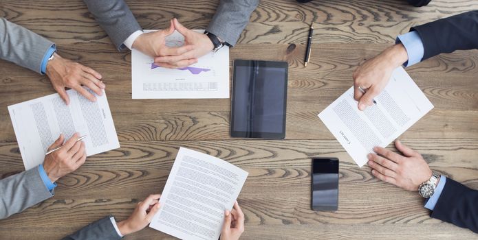 Top view of confident business men in suits sitting at wooden table and discussing new contract terms before signing it top view