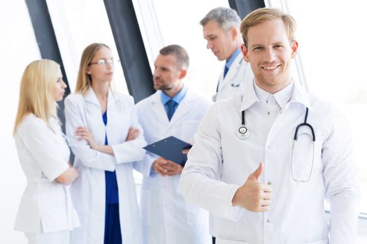 Team of medical professionals, young doctor looking at camera, smiling, showing thumb up