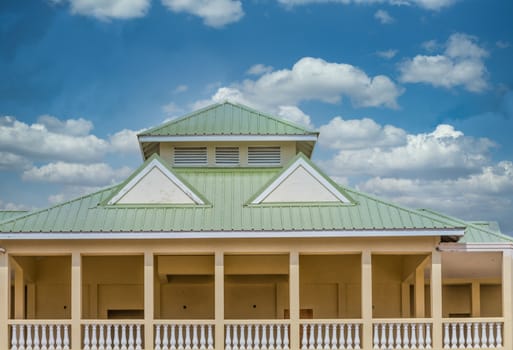 A green metal roof on a yellow plaster building under cloudy sky