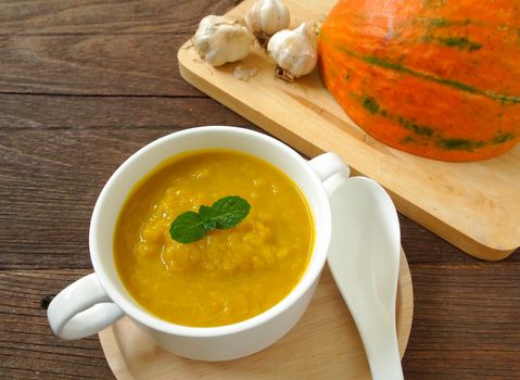 Pumpkin soup in a cup placed on a wooden table.