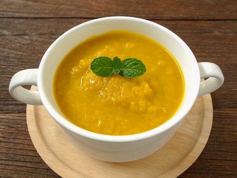 Pumpkin soup in a cup placed on a wooden table.