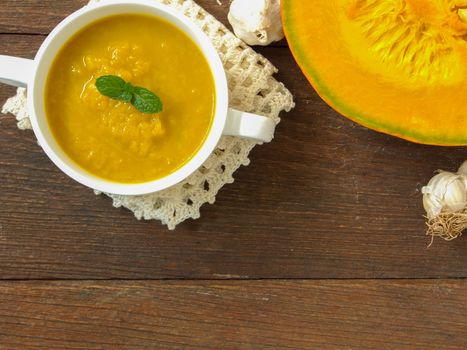 Pumpkin soup in a cup placed on a wooden table.