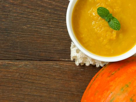 Pumpkin soup in a cup placed on a wooden table.