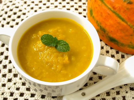 Pumpkin soup in a cup placed on a wooden table.