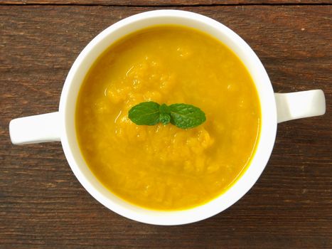 Pumpkin soup in a cup placed on a wooden table.