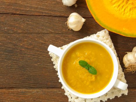 Pumpkin soup in a cup placed on a wooden table.