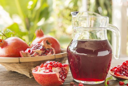Jug of pomegranate juice with fresh fruits on wooden table.