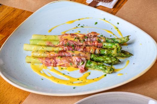 Asparagus roasted in Parma ham in hollandaise sauce and sprinkled with parsley