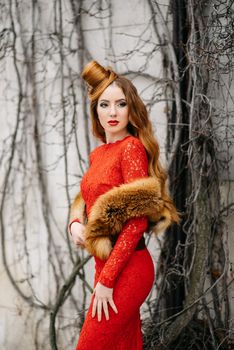 young girl with red hair in a bright red dress near a tree in an empty park