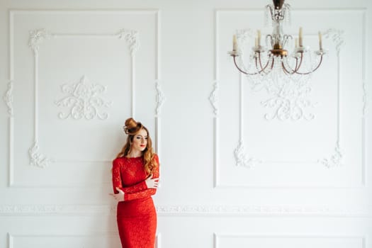 young girl with red hair in a bright red dress in a light room near a white wall