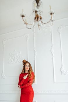 young girl with red hair in a bright red dress in a light room near a white wall