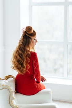 young girl with red hair in a bright red dress in a bright room on an antique sofa