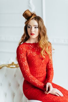 young girl with red hair in a bright red dress in a bright room on an antique sofa