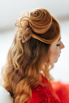 young girl with red hair in a bright red dress in a light room near a white wall