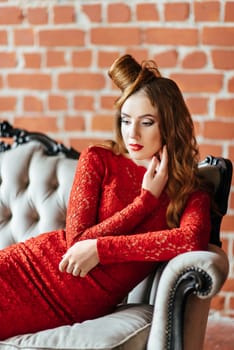 young girl with red hair in a bright red dress in a bright room on an antique sofa