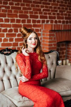 young girl with red hair in a bright red dress in a bright room on an antique sofa