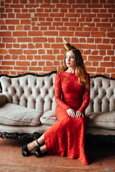 young girl with red hair in a bright red dress in a bright room on an antique sofa