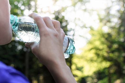 Woman drinking mineral water and resting while jogging in the park