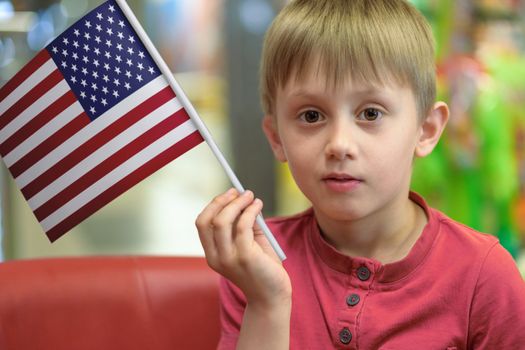 Little boy as a patriot holding in his hand a  paper flag of The United States of America.