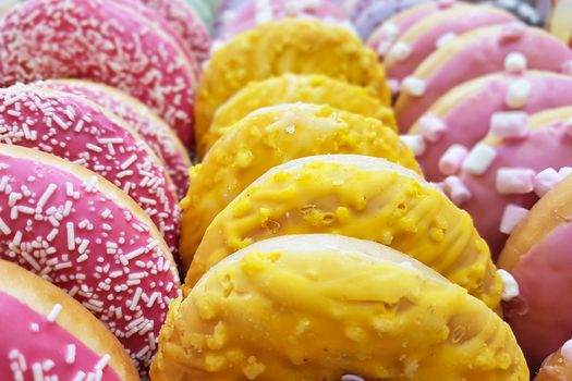 Appetizing multi-colored glazed donuts in rows for sale in a pastry shop in close-up.