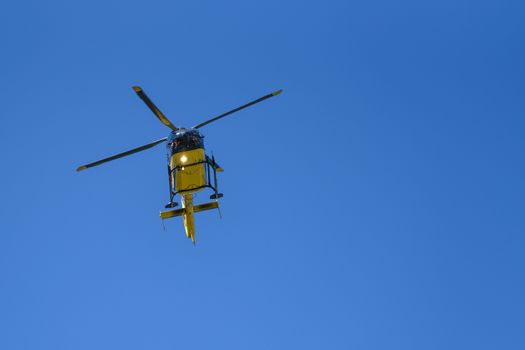 Generic yellow helicopter used for firefighting and rescue operations on the blue sky background - low angel view.