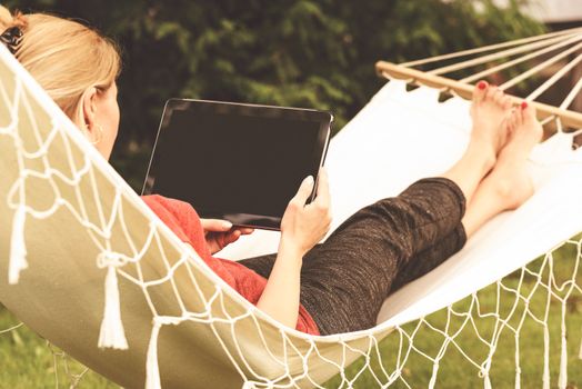 Beautiful woman relaxing on a hammock with and using digital tablet(vintage effect).