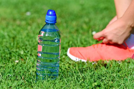 Break in training - mineral water on the grass and woman lacing shoes on the background.