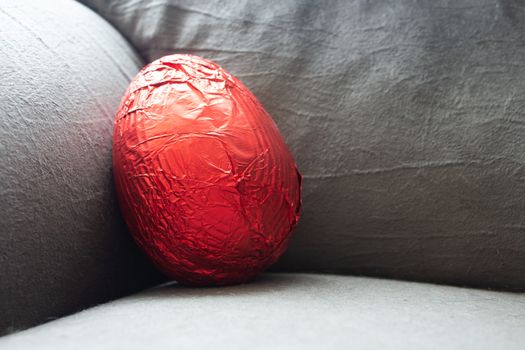 Red easter egg on the corner of a couch still unwrapped