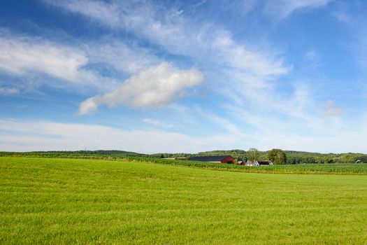 Idyllic landscape of agricultural fields with farm buildings on a background of blue sky and clouds
