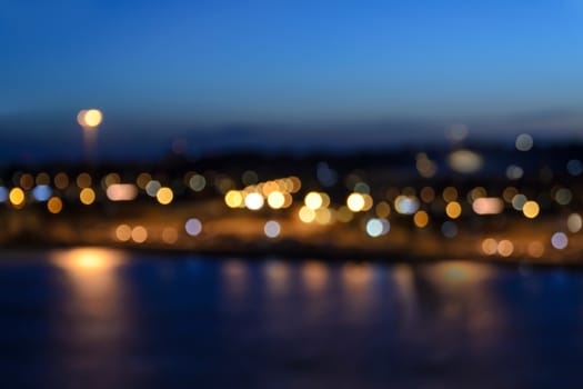 Lights of city coastline with beautiful bokeh effect on the blue sky background in the evening.