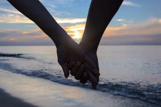 Woman and man in love holding their hands on the beach at sunset.